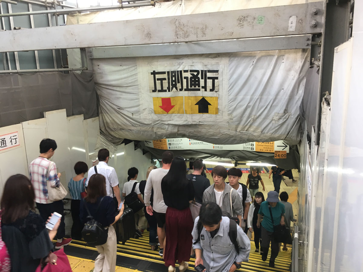 forensen lopen de trap af een metrostation in verbouwing in. Er staan grote Japanse tekens op een doek